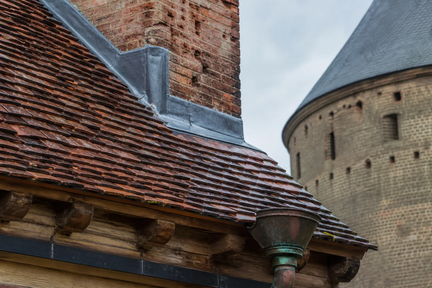 Detail van oude rode dakpannen, loodwerk en een koperen hemelwaterafvoer