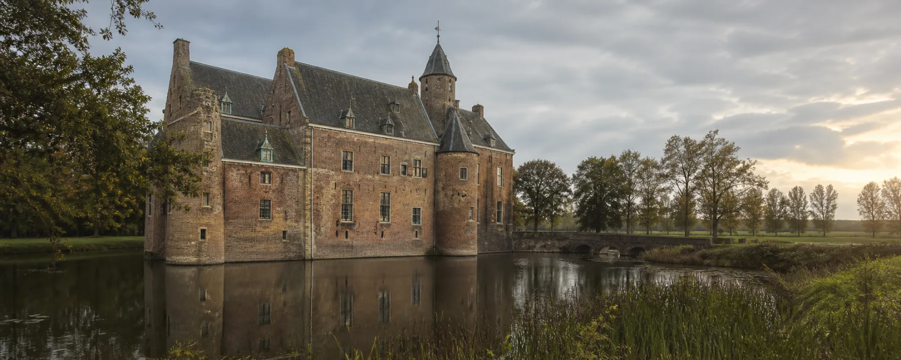 Historisch bakstenen kasteel aan een gracht in het Nederlandse landschap